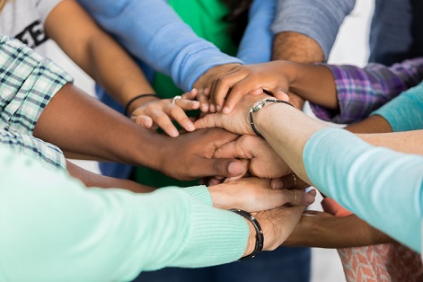 Diverse group of people put hands together in team building exercise. View is of hands and arms only.